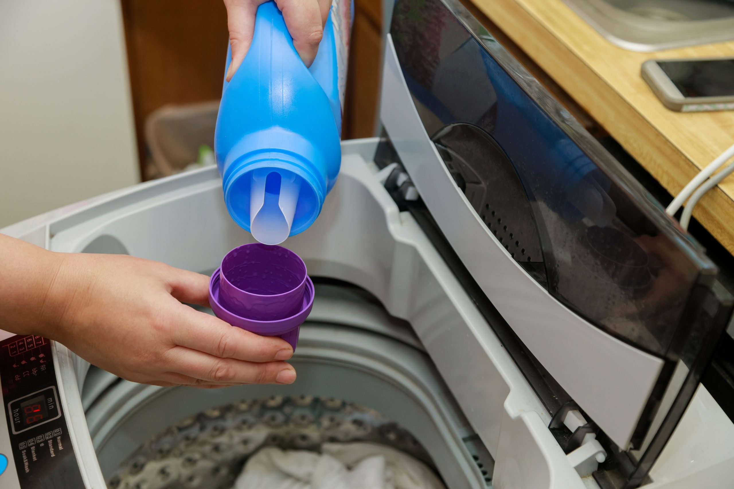 person adding laundry detergent to their washing machine and laundry