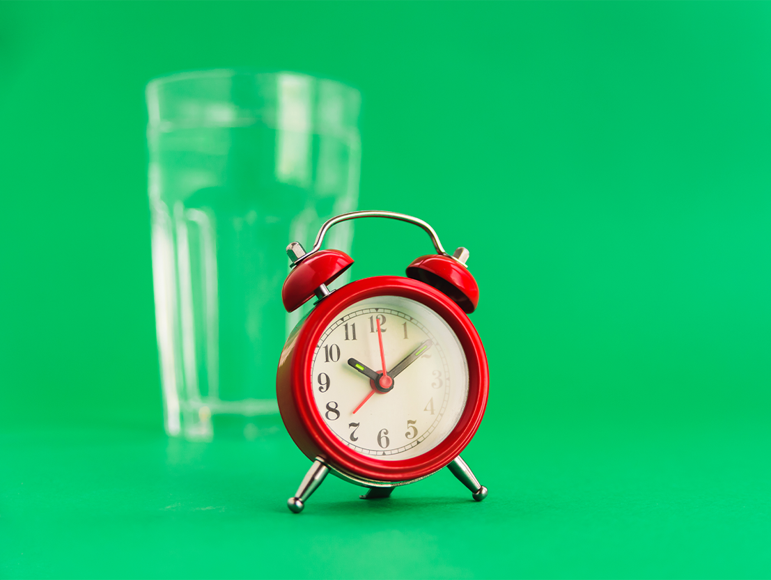 glass of water with a red clock and a green background