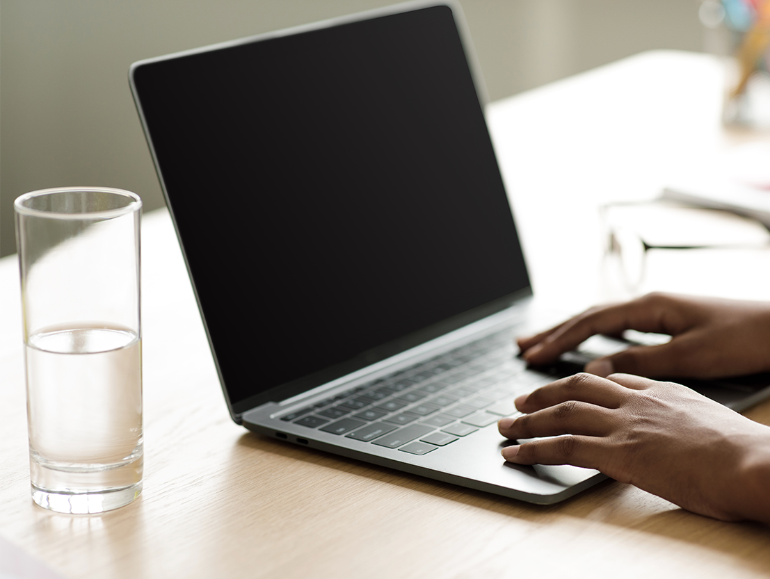 person typing on computer with glass of water next to the computer